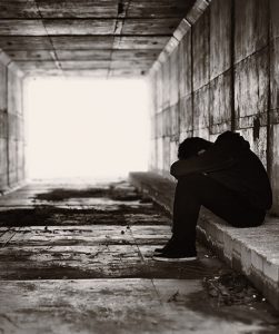 Een jongen zicht in een verlaten tunnel op een stoepje, met zijn handen om zijn benen geslagen. Zijn hoofd rust op zijn onderarmen.